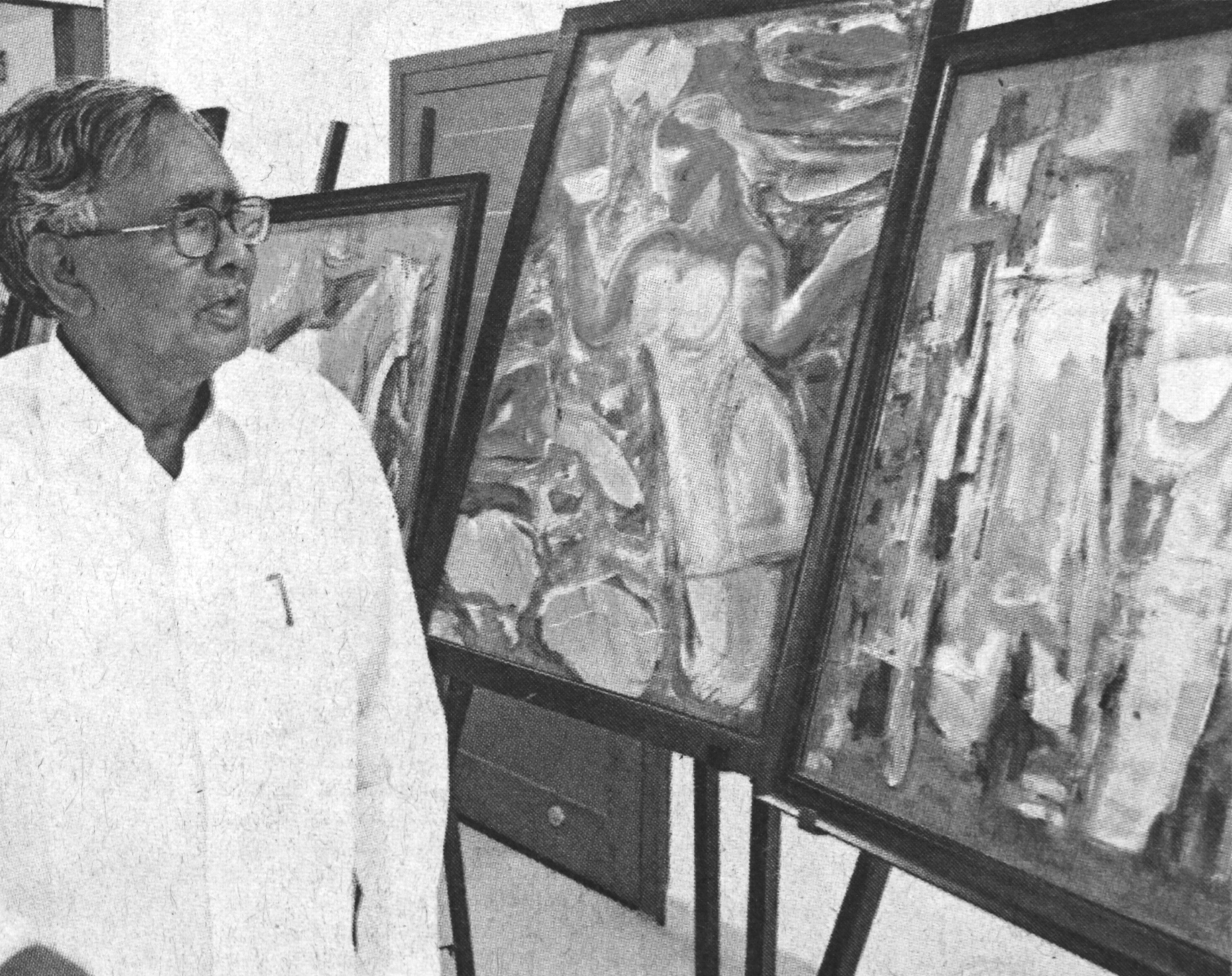 K.S. Vass standing beside paintings in a gallery